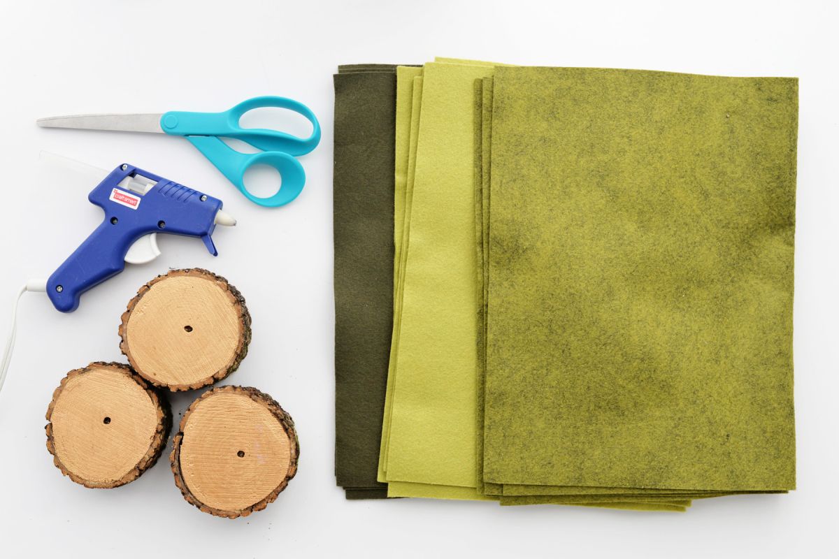 Scissors, wood slices, hot glue gun, and green felt for making felt christmas trees.